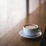Latte on a wooden counter beside a rain-streaked window