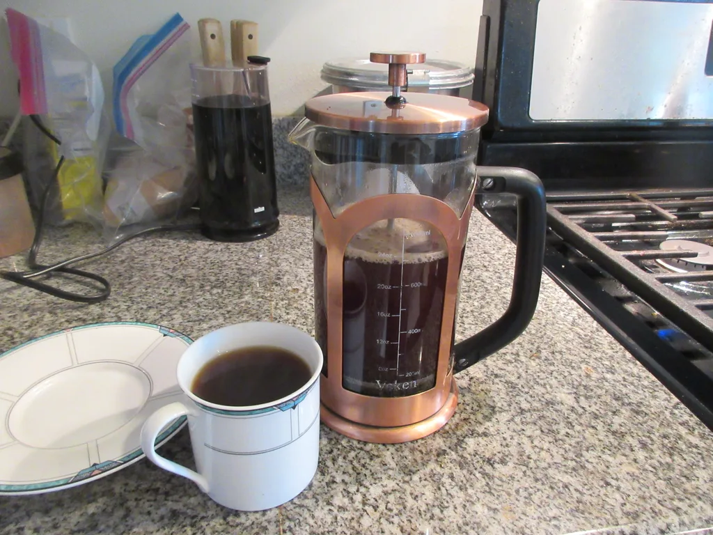 French Press Sediment: Causes & Solutions for a Cleaner Cup 1 Copper French press next to a cup of brewed coffee on a kitchen counter