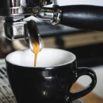 Espresso pouring from a portafilter spout into a black cup