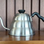 Stainless steel gooseneck pour-over kettle on a wooden shelf